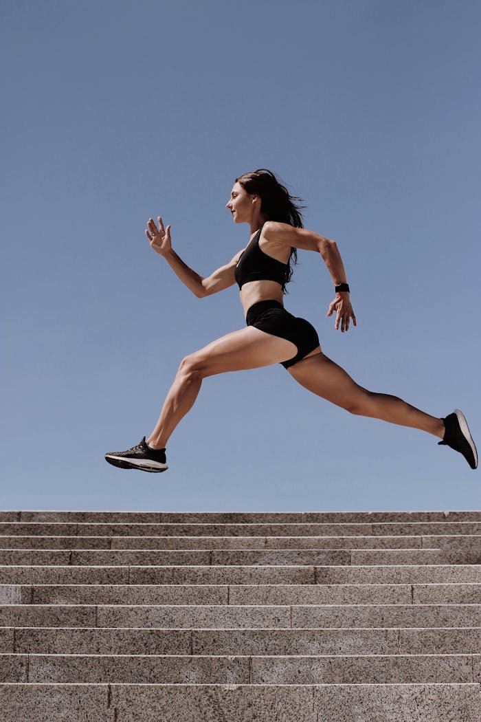 Energetic woman in active wear jumping on stairs outdoors, showcasing fitness and determination.